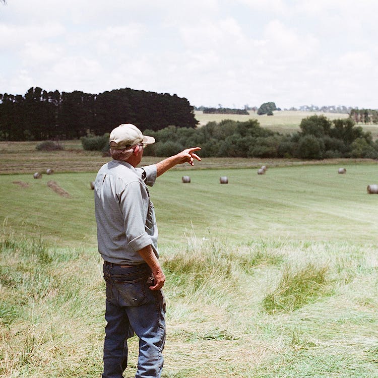 A farmer standing in a green field pointing toward the right